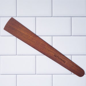May include: A long, thin, wooden spatula with a rounded edge. The spatula is brown and has the text "EARLYWOOD" engraved on it.