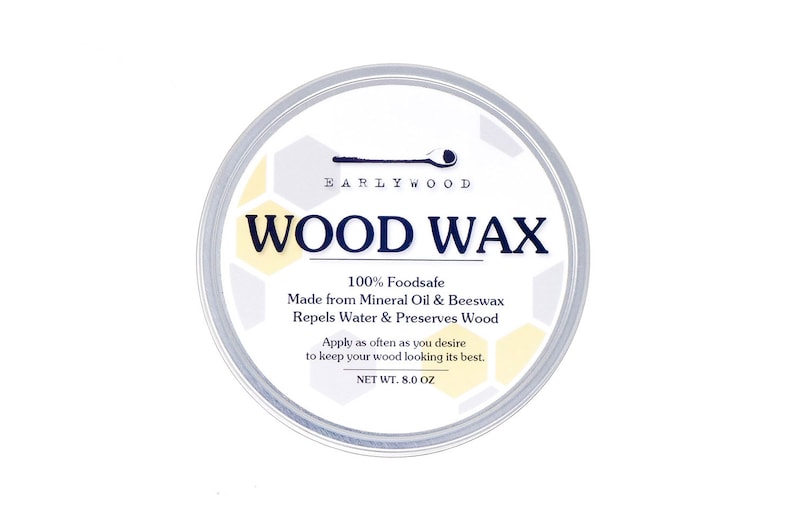 May include: A white round container with a silver lid. The label reads "EARLYWOOD WOOD WAX" and states that it is 100% foodsafe, made from mineral oil and beeswax, repels water and preserves wood. The label also states "Apply as often as you desire to keep your wood looking its best." and "NET WT. 8.0 OZ".