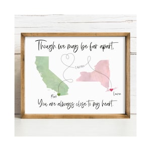 May include: A framed print featuring a green watercolour map of California and a pink watercolour map of New York. A dotted line connects them in a heart shape with the text 2,468 Miles. The text reads Though we may be far apart, You are always close to my heart, with the names Mark and Lauren.