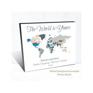 May include: A framed world map print with the text "The World is Yours." The map is colored in shades of blue, gray, and tan. Below the map are the words "Alexander Joseph Martin," "Bachelor of Engineering - University of Maryland," and "May 2026."