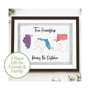 May include: A framed wall art print featuring the text True Friendship Knows No Distance. The design displays three watercolor-style US state maps in purple, blue, and red, connected by dotted lines forming heart shapes with names written nearby.