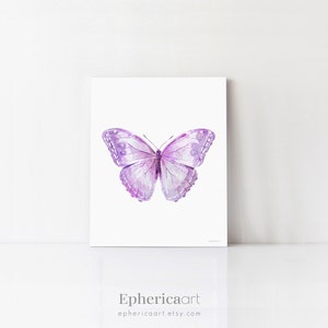 May include: A framed print featuring a watercolor illustration of a butterfly. The butterfly has a symmetrical design with shades of purple and lavender. The artwork is set against a white background. The text "Ephericaart" and the Etsy shop URL are at the bottom.