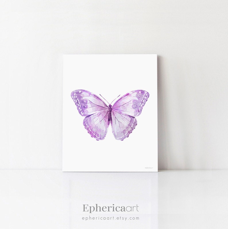 May include: A framed print featuring a watercolor illustration of a butterfly. The butterfly has a symmetrical design with shades of purple and lavender. The artwork is set against a white background. The text "Ephericaart" and the Etsy shop URL are at the bottom.