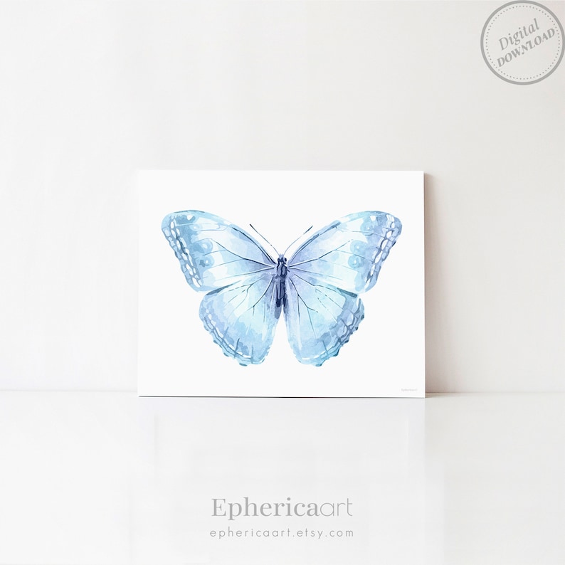 Op de afbeelding: Een aquarelillustratie van een vlinder in lichtblauwe en witte tinten. De vlinder is gecentreerd op een witte rechthoekige achtergrond. In de rechterbovenhoek staat een cirkelvormige stempel met Digital Download. De tekst Ephericaart staat eronder.