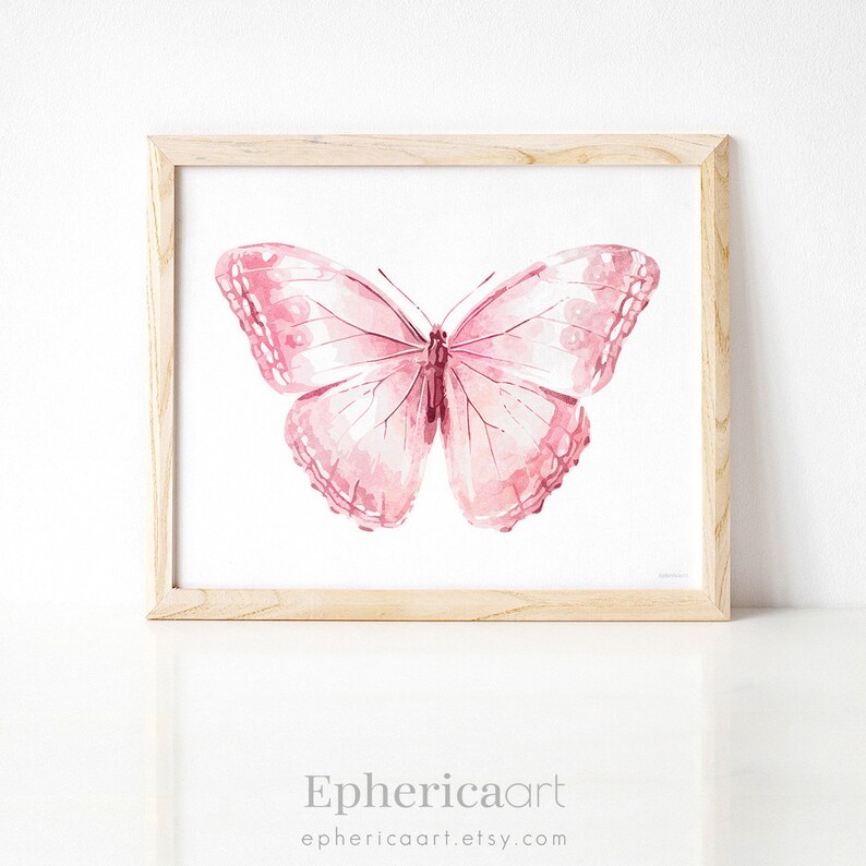 May include: A framed watercolor print featuring a pink butterfly with detailed wing patterns. The butterfly is centered on a white background, set within a light wood frame. The print includes the text "Ephericaart" and the website address.