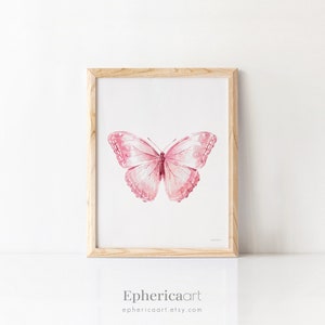 May include: A framed watercolor print featuring a pink butterfly. The butterfly has detailed wing patterns and is centered on a white background. The frame is made of light-colored wood. The artist's name and shop URL are printed at the bottom.