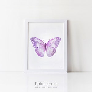 May include: A framed watercolor print of a butterfly. The butterfly is depicted with shades of purple and lavender, with detailed wing patterns. The artwork is set against a white background within a white frame. The artist's name and Etsy shop URL are at the bottom.