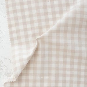 May include: A piece of beige and white gingham fabric. The fabric is folded, showing the pattern and texture. The word "FABLEISM" is printed in the bottom right corner.
