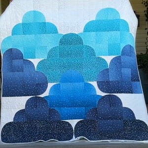 May include: A white quilt with a blue and white cloud design. The clouds are made of different shades of blue and white fabric and are arranged in a pattern.