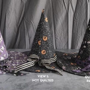 May include: Three conical hats with wide brims. The left hat is purple with a quilted pattern and black ribbon. The center hat is black with orange pumpkin prints and a striped ribbon. The right hat is black with a quilted patchwork top and purple ribbon.