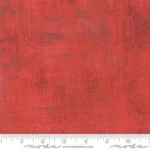 May include: Red fabric with a textured, distressed appearance. The fabric has a mottled effect with darker, brownish-gray streaks and a ruler along the bottom edge. The fabric is suitable for quilting and other craft projects.