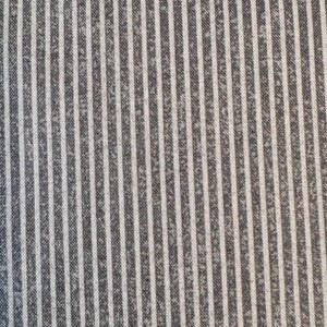 May include: Close-up of a fabric with a vertical striped pattern. The stripes alternate between a dark gray and white color. The fabric has a slightly textured appearance.