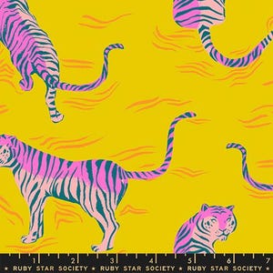 May include: A mustard yellow fabric featuring a repeating pattern of pink tigers with dark teal stripes. The tigers are depicted in various poses, including walking and sitting. A black ruler at the bottom shows 7 inches of length.