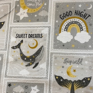 May include: A gray and white fabric with a repeating pattern of squares. Each square features a different design, including a crescent moon, a whale, a rainbow, and a star. The text "Dreams really do come true", "Good Night", "Sweet Dreams", "Stay Wild", and "Moon Child" is printed on the fabric.