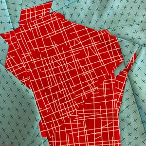 May include: A red fabric with a white grid pattern is layered on top of a blue fabric with a white cross pattern. The red fabric has a geometric shape.