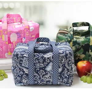 May include: Three insulated lunch bags with different patterns. The first bag is pink with a floral pattern, the second bag is blue with a paisley pattern, and the third bag is camouflage green with a dinosaur pattern.