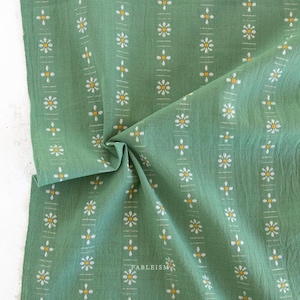 May include: A folded piece of green fabric with a repeating pattern of white and yellow floral designs. The fabric has vertical stripes and the word "FABLEISM" is visible in the bottom right corner.