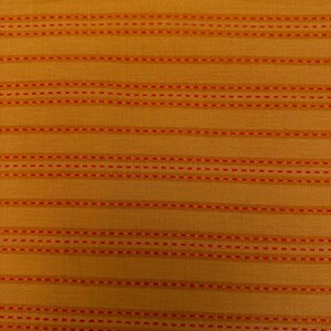May include: Close-up of a textured fabric with a golden-yellow base. Horizontal rows of small, evenly spaced red dashes create a striped pattern across the material. The fabric has a subtle sheen.