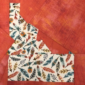 May include: A quilt block featuring a patchwork design of a state outline in a white fabric with a pattern of colorful feathers on a red background.