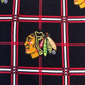 May include: Black fabric with a red and white plaid pattern. A red, yellow, and green Native American headdress logo is repeated throughout the fabric. The logo includes the letter "R" in a circle.