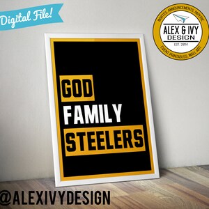 May include: A black and gold printable wall art print with the text "GOD FAMILY STEELERS" in white and yellow letters. The print is framed in a white frame and is sitting on a wooden surface. The text "@ALEXIVYDESIGN" is at the bottom of the print.