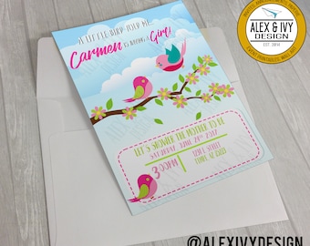 Puede incluir: Una invitación a una fiesta de bienvenida al bebé con un fondo azul y blanco que presenta pájaros rosas y verdes en una rama con flores rosas y amarillas. El texto dice "A little bird told me... Carmen is having a girl!" e incluye la fecha, la hora y la ubicación de la fiesta.