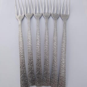 May include: A set of six silver forks with textured handles. Each fork has four tines and a simple design. The handles feature a textured, woven pattern. The forks are arranged in a row on a white surface, suitable for a formal dining occasion.