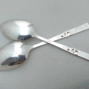 May include: Two silver spoons with ornate floral designs on the handles. The spoons are crossed over each other.