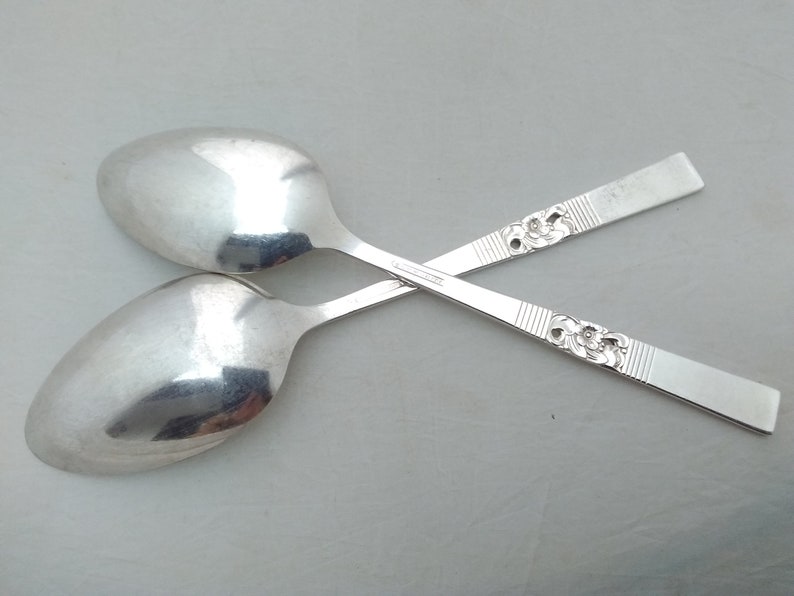 May include: Two silver spoons with ornate floral designs on the handles. The spoons are crossed over each other.