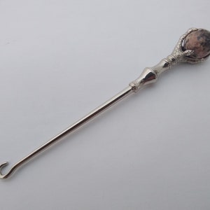May include: A silver metal hook with a claw-like handle and a pink and white stone orb at the top.