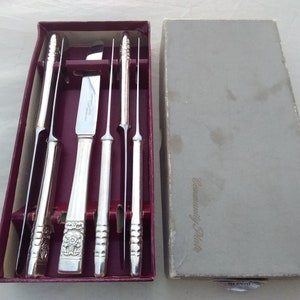 Puede incluir: Un juego de cinco cuchillos para carne plateados en una caja color burdeos con las palabras "Community Plate" impresas en la caja. Los cuchillos est&aacute;n en una caja forrada de terciopelo con ranuras individuales para cada cuchillo.