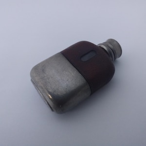 May include: A rectangular pocket flask featuring a two-tone design with a brushed silver metal base and a dark brown wooden upper section. The flask includes a small, centred rectangular viewing window on the wood and a silver screw-top cap.