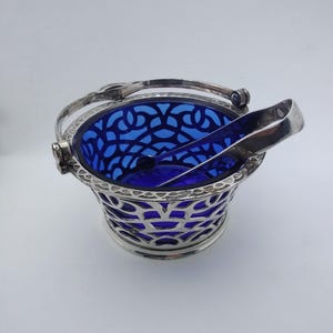 May include: An ice bucket with a cobalt blue interior and a silver filigree exterior. The bucket has a handle and comes with silver tongs. The bucket is designed to hold ice and chill beverages.