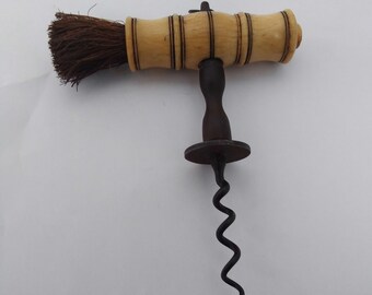 May include: Antique corkscrew with a bone handle and a brush attached. The corkscrew is made of metal and has a spiral shape.