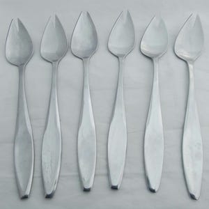 May include: Set of six silver-toned serving spoons with a unique, slightly curved design. Each spoon has a two-pronged fork at the end.