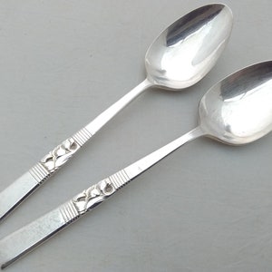 May include: Two silver spoons with ornate designs on the handles. The spoons have a polished finish and are in good condition.