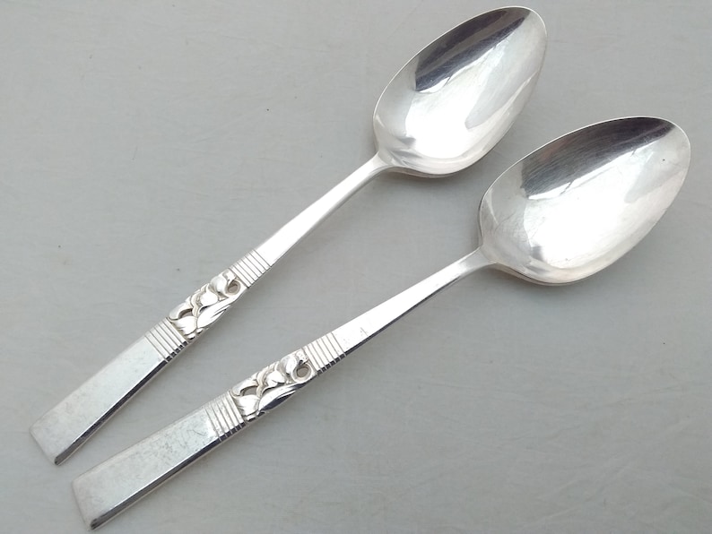 May include: Two silver spoons with ornate designs on the handles. The spoons have a polished finish and are in good condition.
