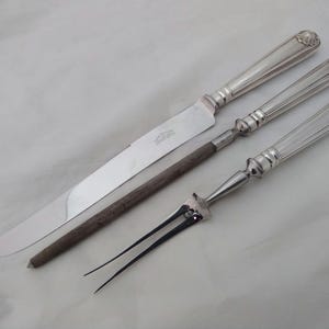 May include: A silver carving set with a knife, fork, and a wooden handle. The knife has a silver handle with a decorative pattern.