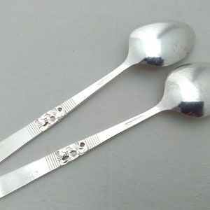 May include: Two silver spoons with ornate floral designs on the handles. The spoons are lying on a white surface.