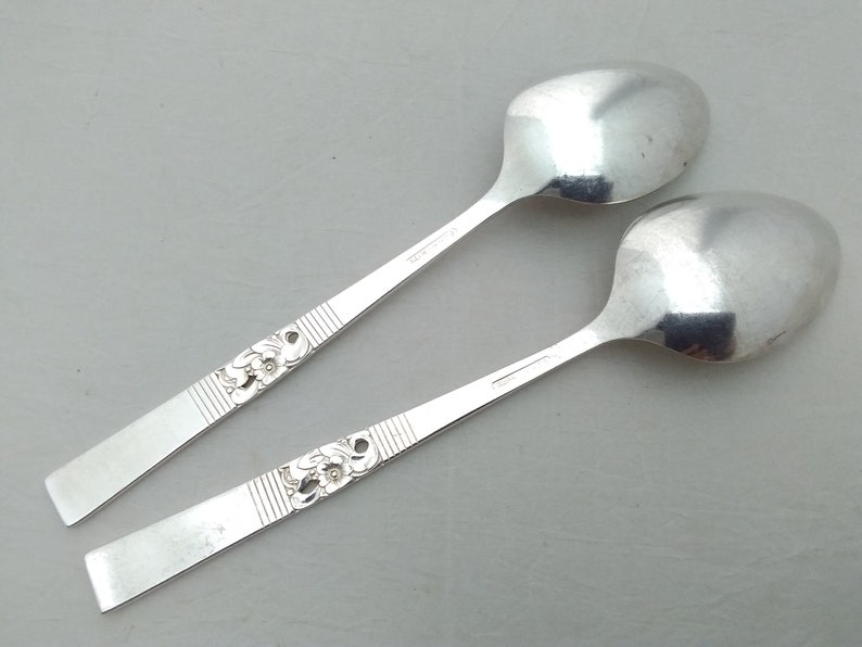 May include: Two silver spoons with ornate floral designs on the handles. The spoons are lying on a white surface.