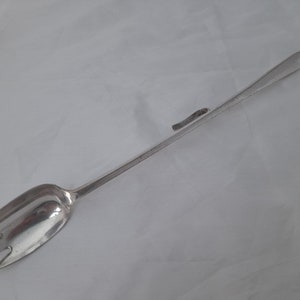 May include: A silver serving utensil with a long handle and a spoon-shaped head with a fork at the end.