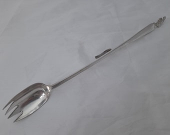 May include: A silver serving utensil with a long handle and a spoon-shaped head with a fork at the end.