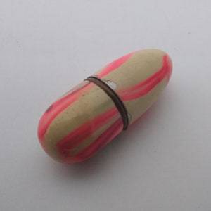 K&ouml;nnte beinhalten: Eine kleine, cremefarbene Pillendose mit rosa Streifen. Die Pillendose ist aus Kunststoff und hat einen Klappdeckel.