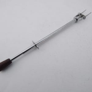 May include: A chrome-plated cake lifter with a dark brown wooden handle. The lifter has a long, slender body with a circular grip and two prongs at the end. The handle is approximately 1 inch in diameter.