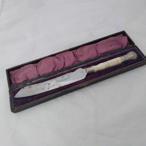 May include: A silver and ivory handled knife in a purple velvet lined box.