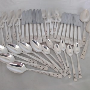 May include: A set of silver-coloured cutlery, including forks, knives, and spoons. The utensils have decorative handles with an ornate design. The spoons are oval-shaped, and the knives have a smooth, silver blade.