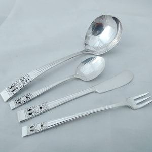 May include: A set of four silver-plated serving utensils, including a ladle, a butter knife, a serving spoon, and a serving fork. The utensils have an ornate design with floral motifs.
