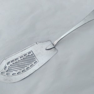May include: A silver serving utensil with a decorative, openwork design. The utensil has a long handle and a wide, flat blade.