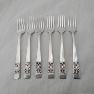 May include: Six silver forks with ornate handles. The forks feature a decorative design with a floral motif.