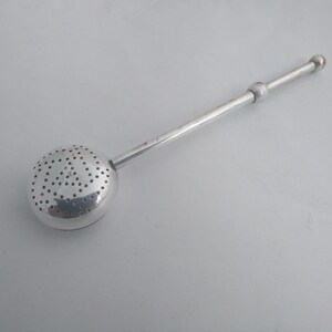 May include: A silver tea infuser with a perforated spherical basket and a long handle. The handle has a small ball in the middle and a red-tipped end. Designed for steeping loose leaf tea.